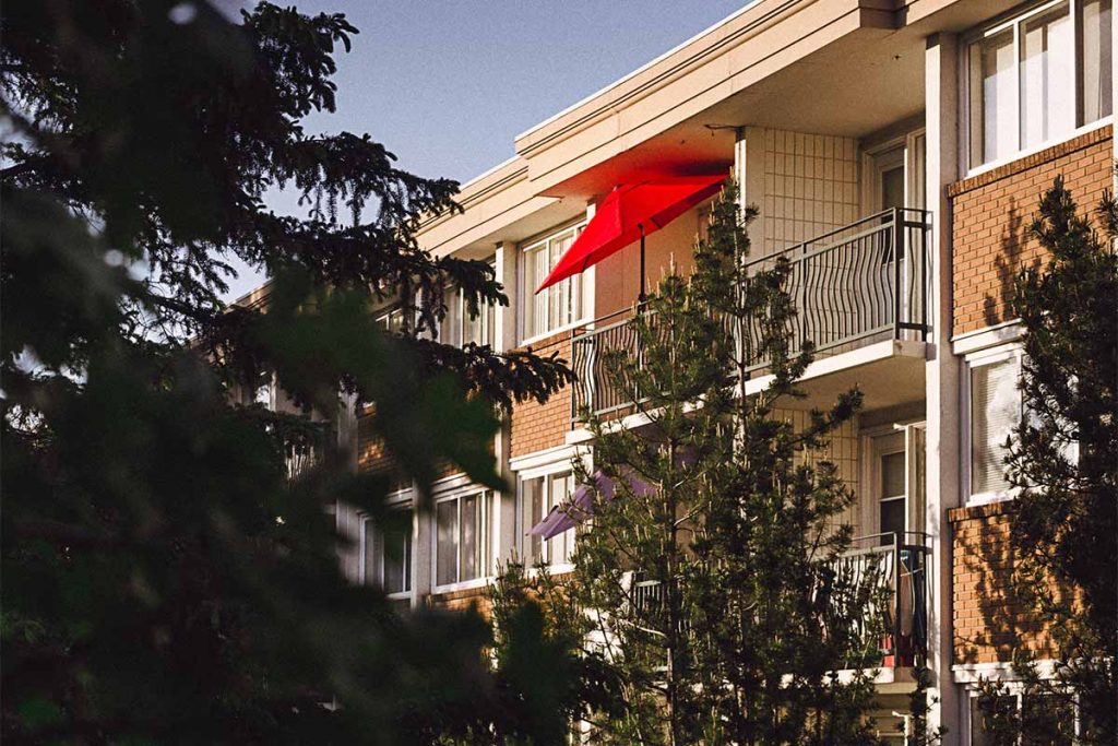 apartment building with trees and red umbrella on the balcony