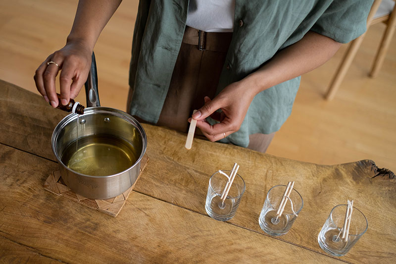 Person holding popsicle stick near candle glass jars