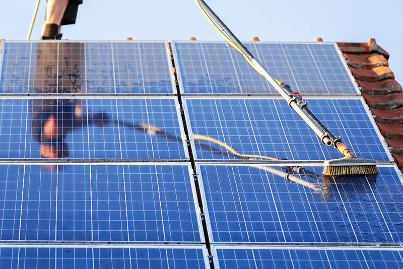 a man cleaning dirty solar panels standing on a roof