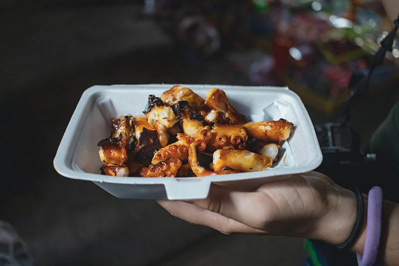 a person holding styrofoam container with cooked food