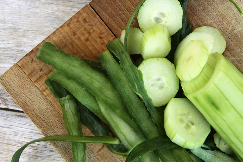 fresh cut cucumber and cucumber peels on a wooden table