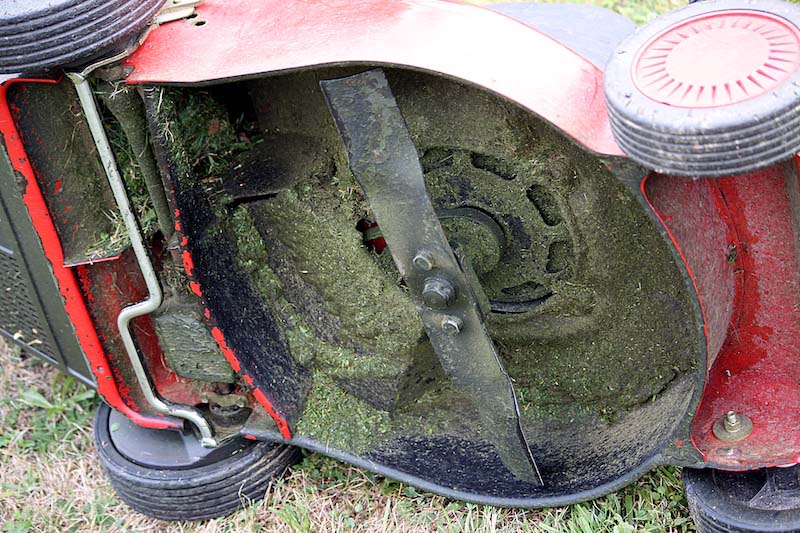 the underside of an electric lawn mower with grass clumped up