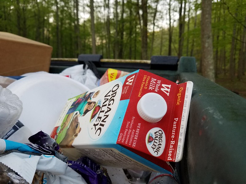 a full trash bin with a milk carton on top