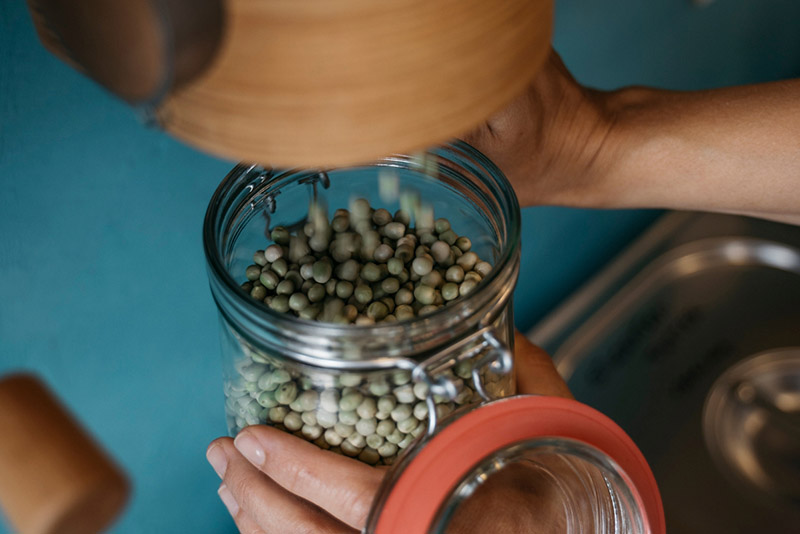 a person pouring dried peas into a glass container to help reduce packaging 