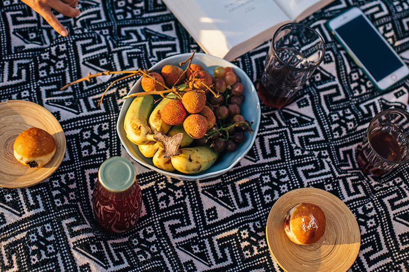 a bowl with fruit and a book on the picnic cloth