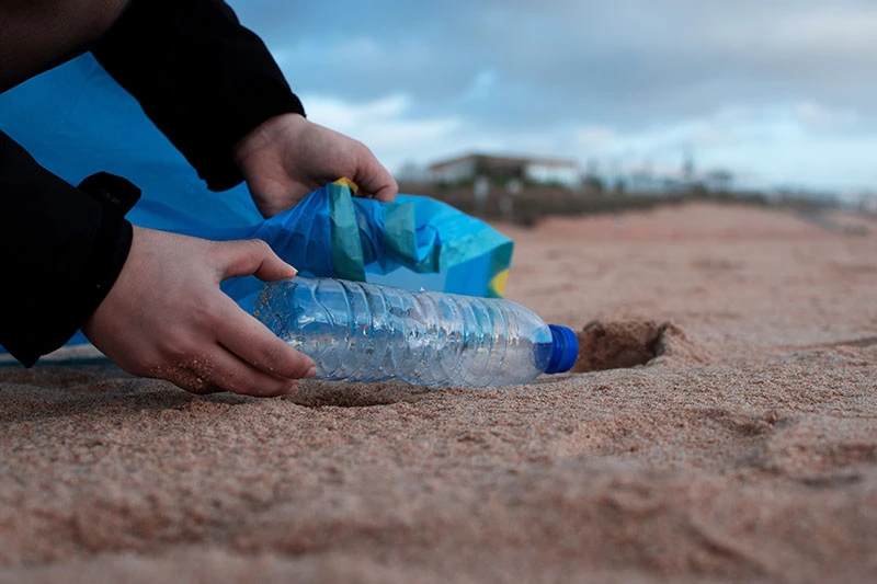 a person picking up plastic bottle from the sand
