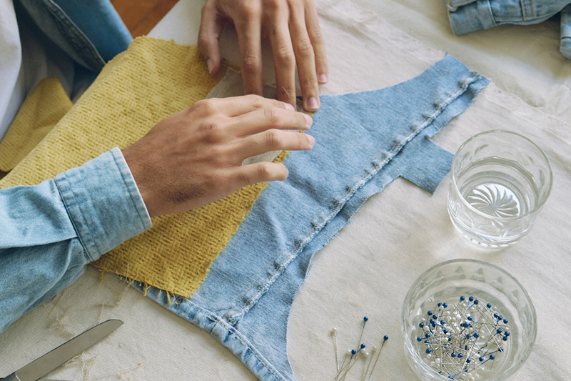 a person sewing a denim clothing item