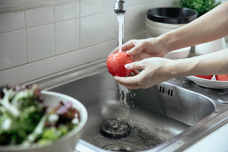 a person washing an apple under running water in the sink